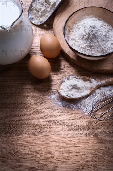 Composition of objects egs spoon corolla milk pitcher flour in bowl and scoop on wooden board