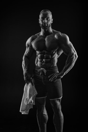 Silhouette of a strong bodybuilder. Confident young fitness athlete with a powerful body and perfect abs. Black and white photography. Dramatic light. Mixed media