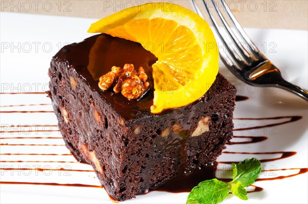 Fresh baked delicious chocolate and walnuts cake with slice of orance on top and mint leaf