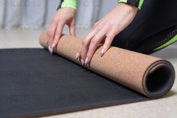 Image of a young woman in a gymnastics suit rolling up a mat after a workout. The concept of fitness