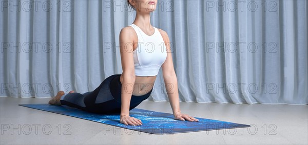 Image of a beautiful woman in a gymnastic suit performing yoga exercises in a bright studio on a mat. Yoga concept. Spiritual practices.Mixed media