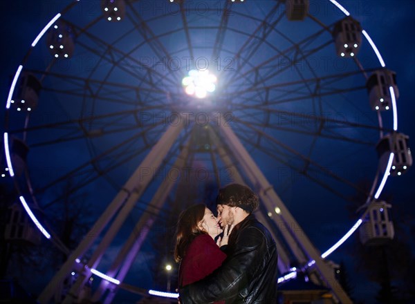 Couple in love in an amusement park near a ferris wheel on a date in cold weather. The concept of love and joy in relationships