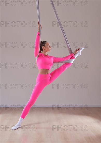 Image of a beautiful woman posing in a bright studio near the hammocks. The concept of airstretching. Fitness and sports