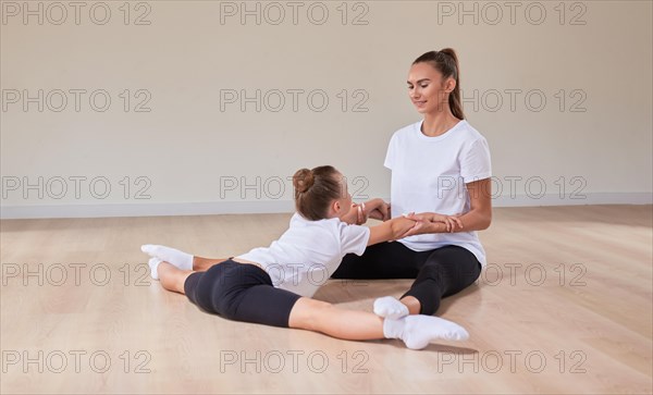 Beautiful female teacher helps a little girl stretch in a gymnastics class. The concept of education