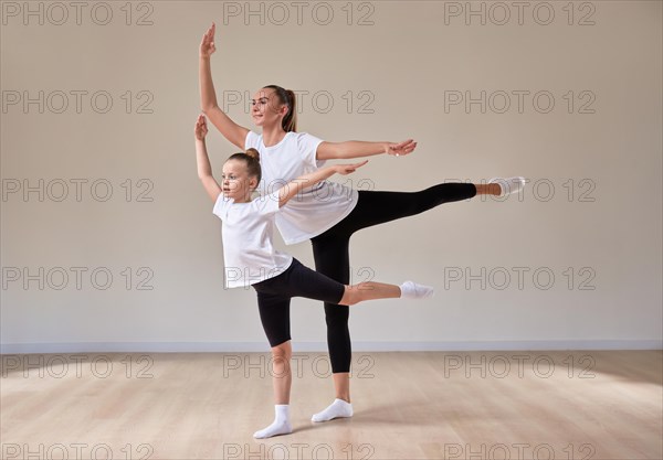 Beautiful woman teacher and a little girl perform dance movements in a bright studio. The concept of education