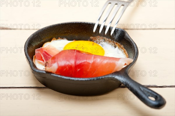 Fried egg sunny side up with Italian tyrolean speck smoked ham on a skillet