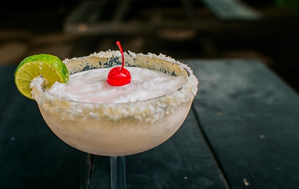 Close up of delicious frozen coconut cocktail with cherry. Frozen coconut margarita with lemon slice served on wooden table