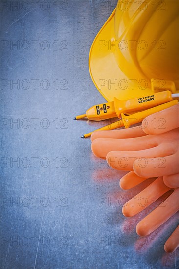 Electricians rubber gloves building helmet electric tester on scratched metallic background electricity concept