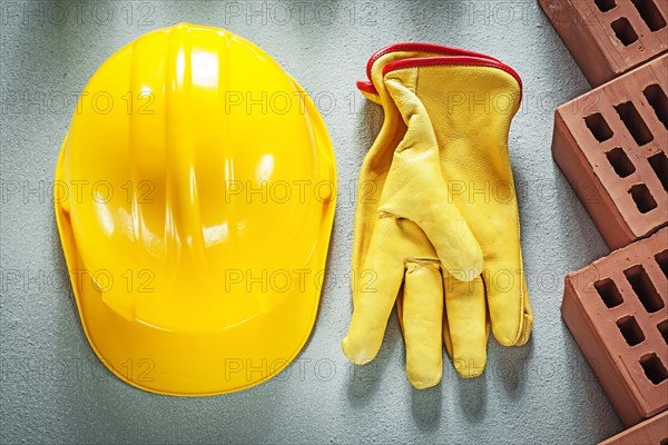 Red building bricks protective hard hat leather safety gloves on concrete background construction concept