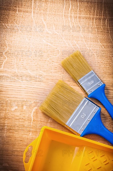 Aerial view two paintbrushes with blue handles and yellow paint can on wooden board construction concept