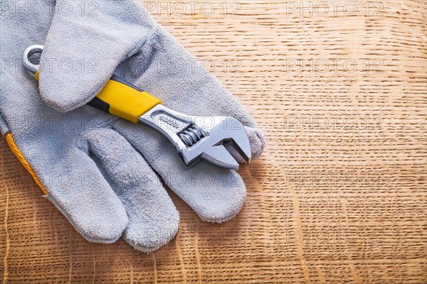 Adjustable spanner in horizontal design and protective work glove on wooden board Construction concept