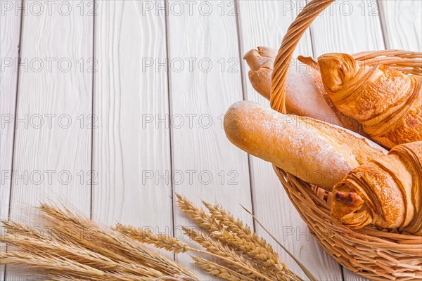 Copyspace image Croissants and baguettes in wicker basket ears of corn on white wooden boards
