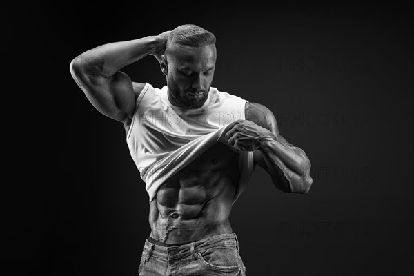 Silhouette of a strong bodybuilder. Confident young fitness athlete with a powerful body and perfect abs. Black and white photography. Dramatic light. Mixed media