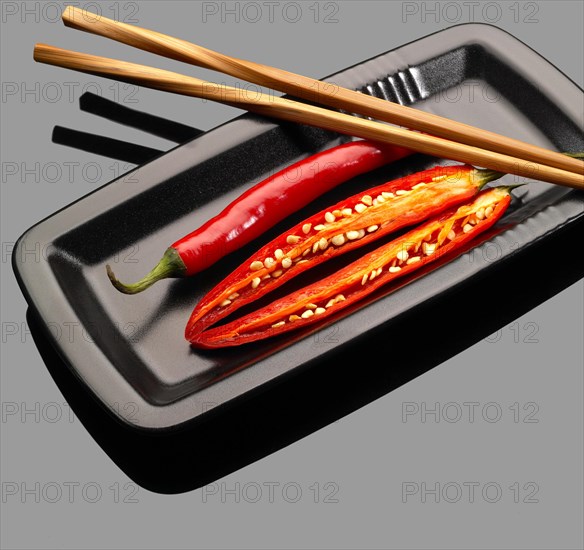 Fresh red chili peppers on a plate with chopstikcs over grey reflective surface