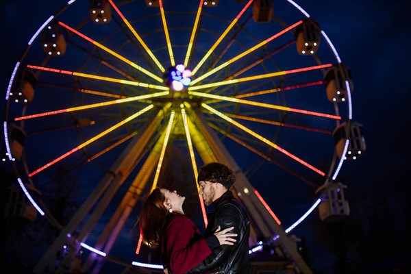 Couple in love in an amusement park near a ferris wheel on a date in cold weather. The concept of love and joy in relationships