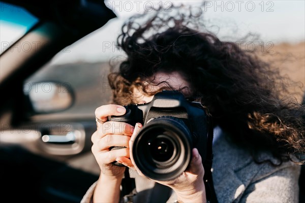 Curly girl in a convertible holds a camera in her hands
