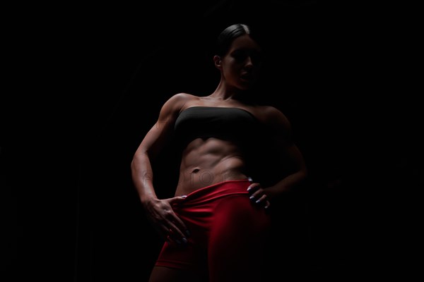 Muscular woman wearing fitness clothing posing against black background. Caucasian female model with perfect abs. Mixed media