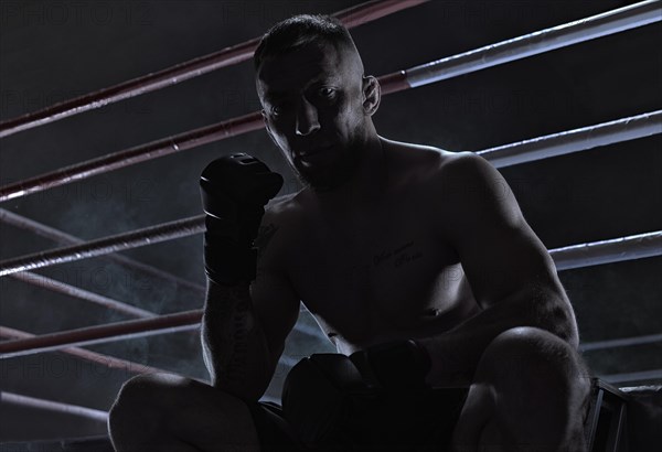 Kickboxer is sitting near the ring and motivatingly shows his fist in the overlay. Sports competitions. Fight night. The concept of mixed martial arts. MMA