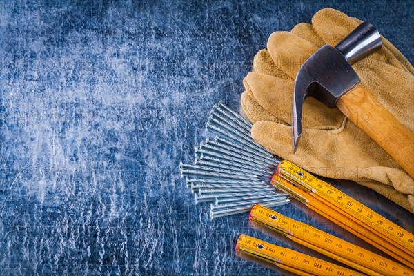 Copy space image of leather working gloves nails wooden measuring meter and claw hammer on scratched metallic background construction concept