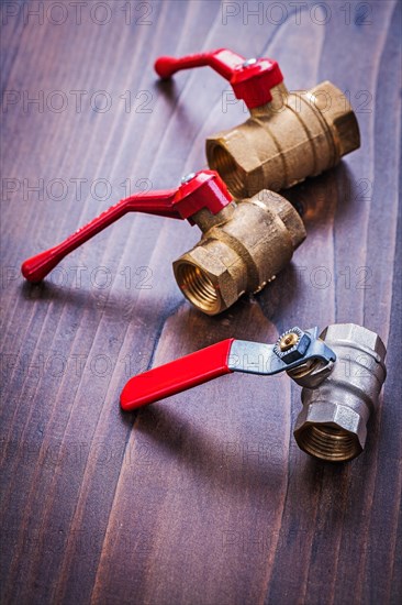 Three plumbing fittings with red handles on an old wooden board