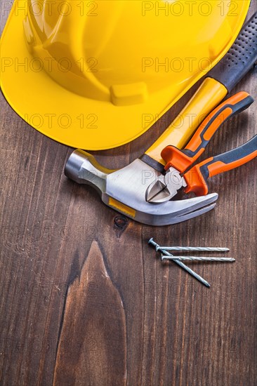 Claw hammer pliers nails yellow helmet on vintage wooden board construction concept