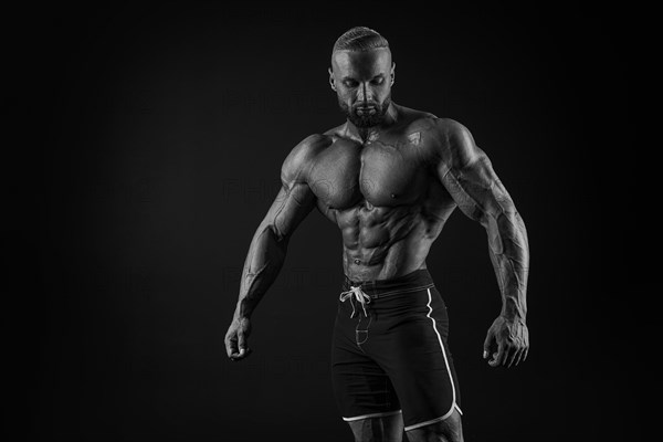 Silhouette of a strong bodybuilder. Confident young fitness athlete with a powerful body and perfect abs. Black and white photography. Dramatic light. Mixed media