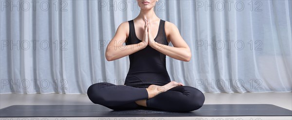 Young woman sits in a lotus position in a bright studio on a black mat. Yoga concept. Women's spiritual practices. Fitness. Mixed media