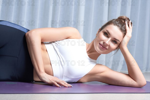 Beauty portrait of a charming woman in a gymnastic suit lying on a mat in a bright studio. The concept of fitness