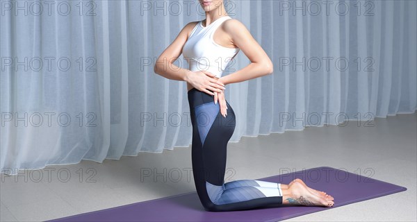 Image of a young woman in a gymnastic suit performing yoga exercises on a mat in a bright studio. The concept of fitness