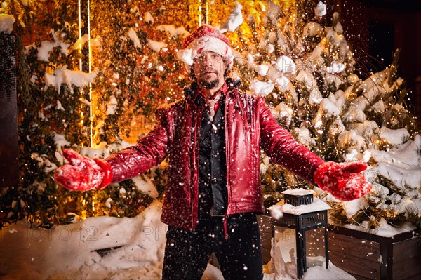 Man dressed as Santa Claus throws up snow on a street decorated with garlands. New Year and Christmas concept. Mixed media