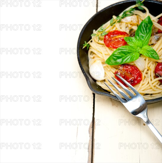 Italian spaghetti pasta with baked tomatoes basil and thyme sauce on a cast iron skillet