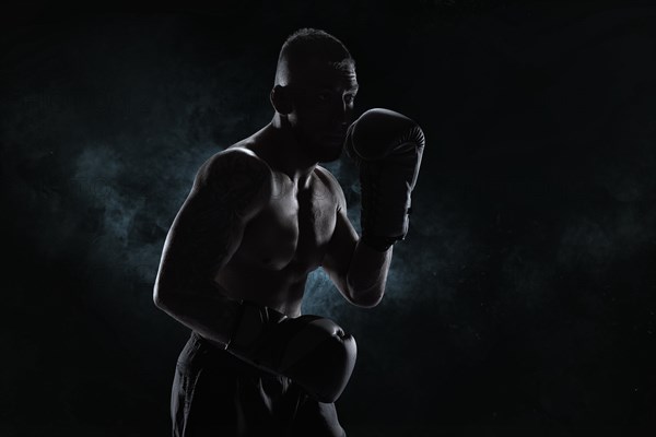 Kickboxer in black gloves posing on a background of smoke. The concept of mixed martial arts. MMA