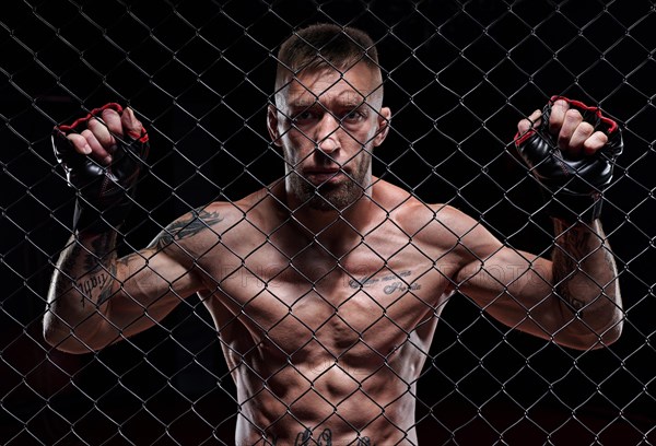 Dramatic image of a mixed martial arts fighter standing in an octagon cage. The concept of sports