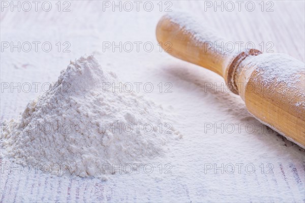 A small pile of natural white flour and a wooden rolling pin