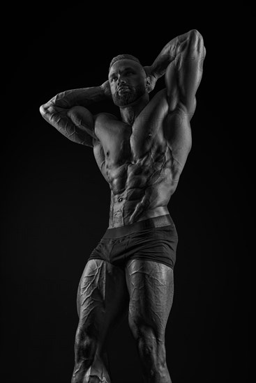 Silhouette of a strong bodybuilder. Confident young fitness athlete with a powerful body and perfect abs. Black and white photography. Dramatic light. Mixed media