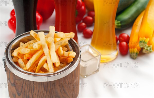 Fresh french fries on a wood bucket with selection of beers and fresh vegetables on background