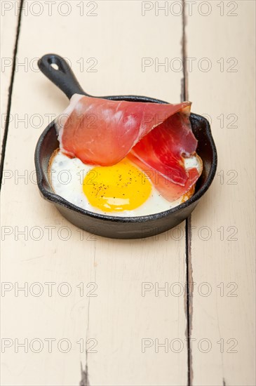 Fried egg sunny side up with Italian tyrolean speck smoked ham on a skillet