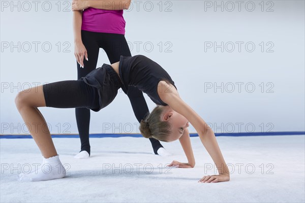 Training in the gym class. A little girl under the guidance of a trainer performs exercises. Gymnastics concept. Mixed media