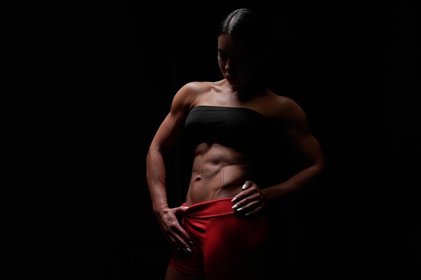 Muscular woman wearing fitness clothing posing against black background. Caucasian female model with perfect abs. Mixed media