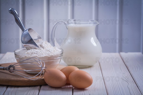 Horizontal version corolla eggs flour bowl scoop pitcher milk on white painted old wooden board food and drink concept