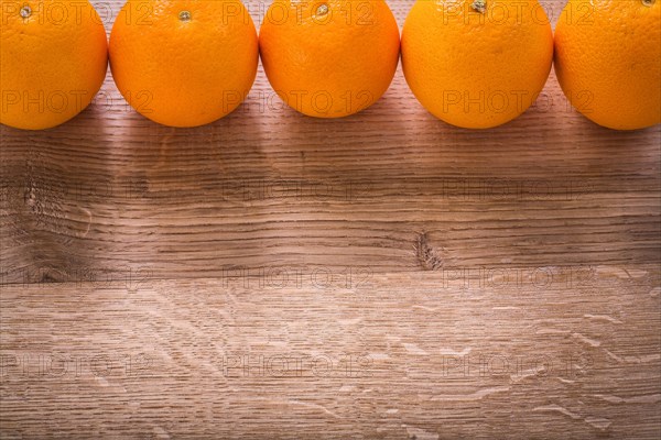 Five oranges organised in row on wooden board