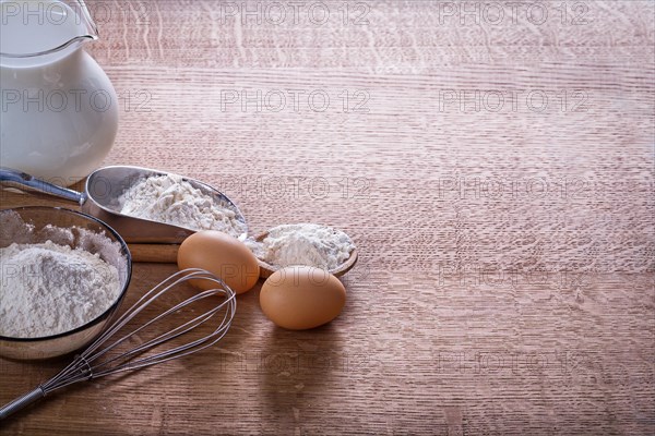 Organised copyspace eggs corolla flour in spoon scoop bowl pitcher milk on wooden board food and drink concept