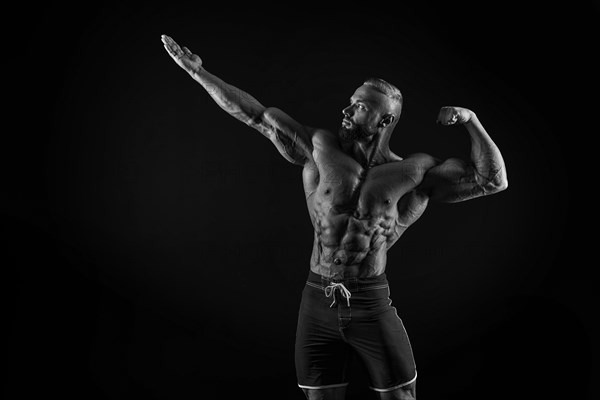 Silhouette of a strong bodybuilder. Confident young fitness athlete with a powerful body and perfect abs. Black and white photography. Dramatic light. Mixed media