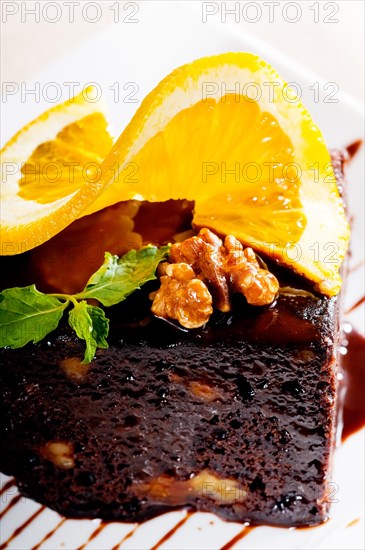 Fresh baked delicious chocolate and walnuts cake with slice of orance on top and mint leaf