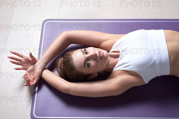 Beauty portrait of a charming woman in a gymnastic suit lying on a mat in a bright studio. The concept of fitness