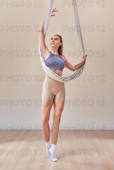 Image of a beautiful woman posing in a bright studio near the hammocks. The concept of airstretching. Fitness and sports