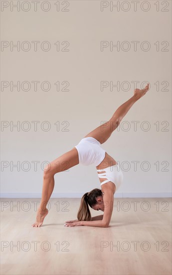 Flexible woman in white sportswear took a bridge position on her hands and gracefully spread her legs. The concept of gymnastics