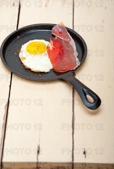 Fried egg sunny side up with Italian tyrolean speck smoked ham on a skillet