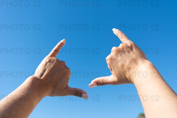 Woman's hands showing surfer sign against blue sky background