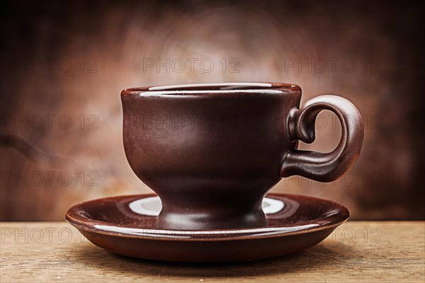 Brown clay coffee cup on saucer on vintage wood background